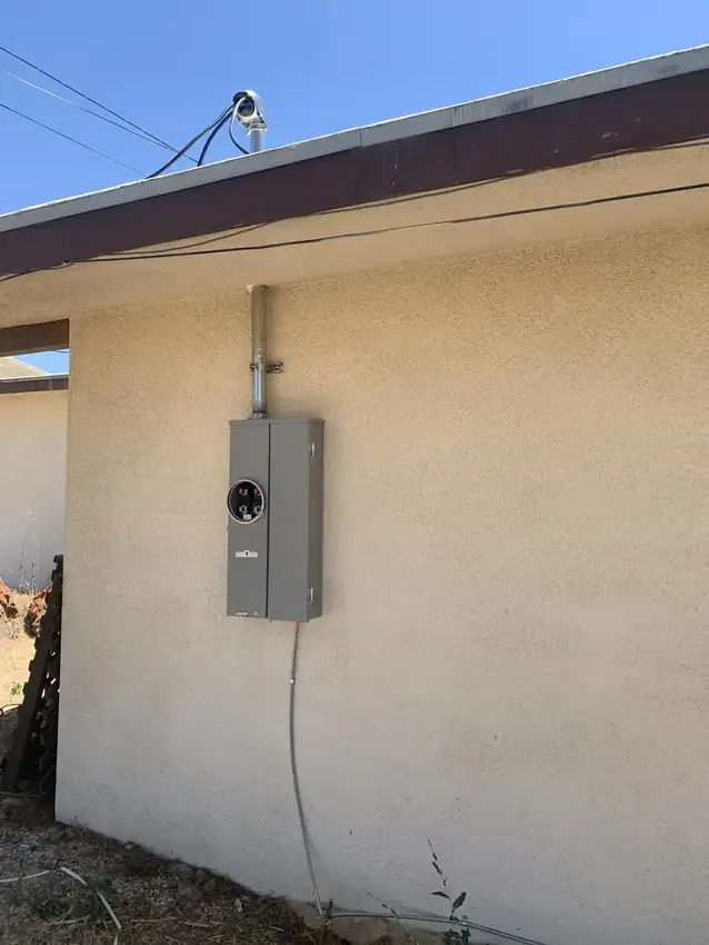 Meter socket and service panel mounted on a stucco exterior wall, with conduit running up to the roofline.